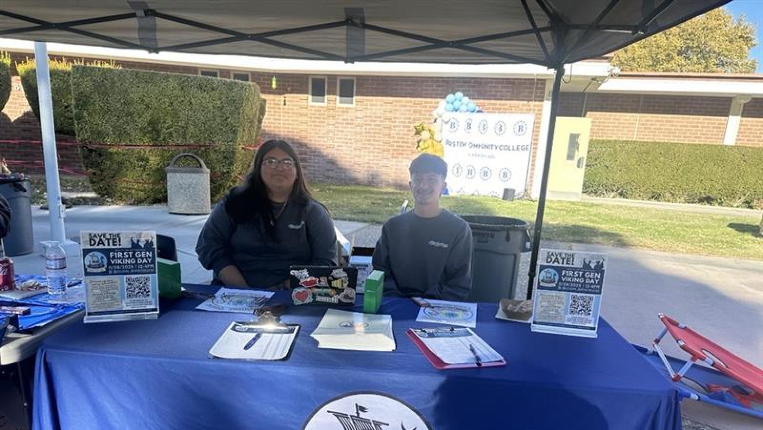 Students sitting in front of a BCC table under a tent
