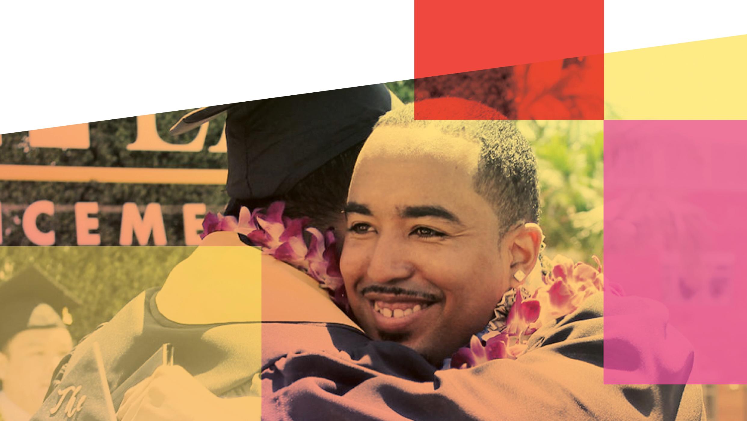 A smiling male graduate wearing a floral lei embraces another person.