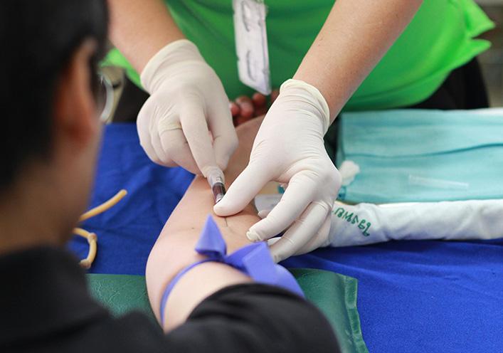  A close-up of a healthcare worker's gloved hands drawing blood from a patient's arm with a needle.